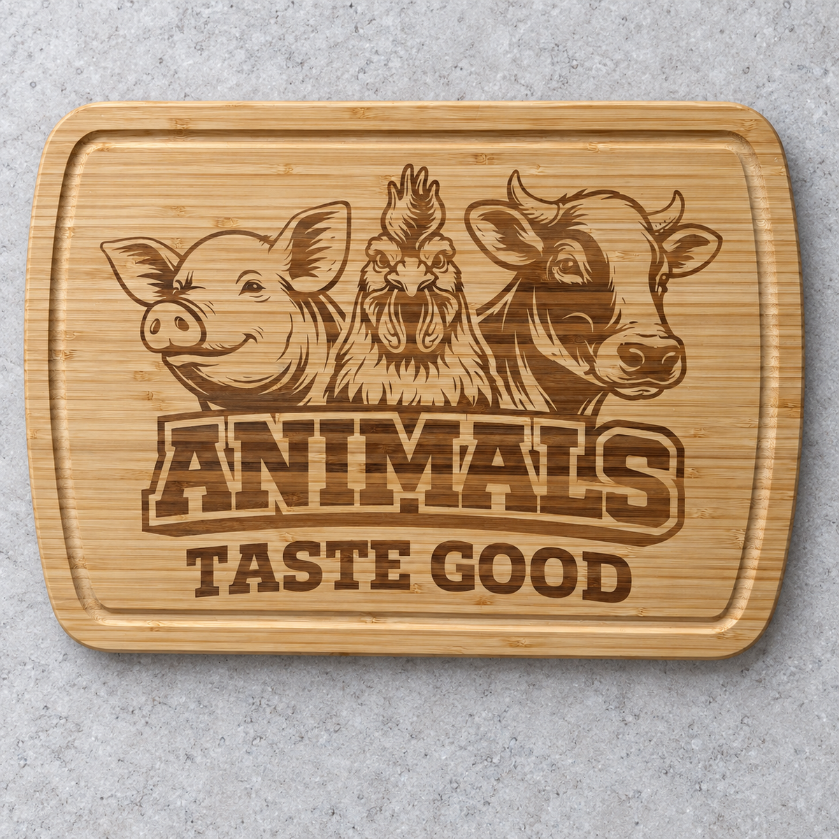 Bamboo cutting board engraved with a pig, rooster and cow above Animals Taste Good, lying on a light stone counter.