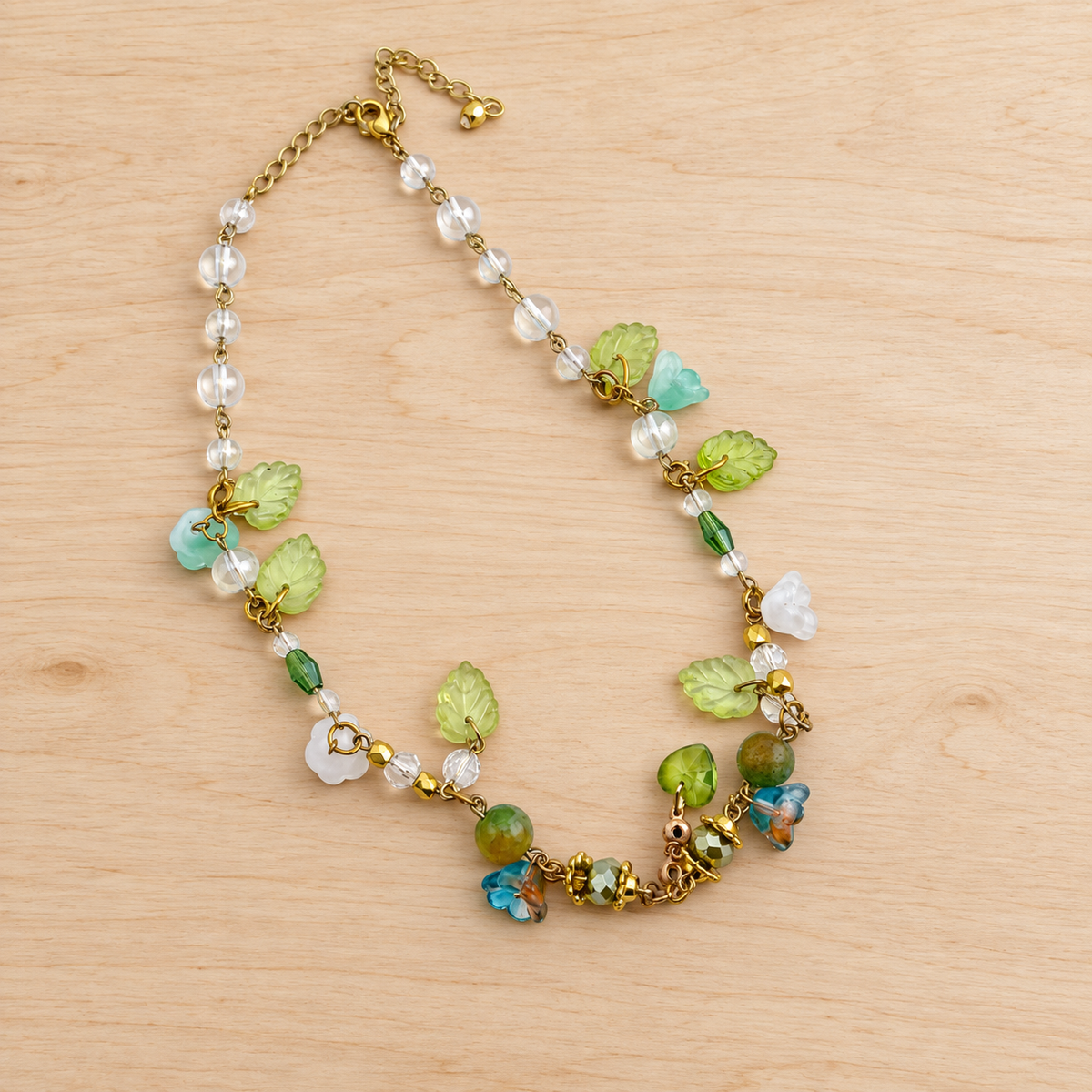 Day's Creations necklace with clear beads, green leaves and flower charms on pale wood.