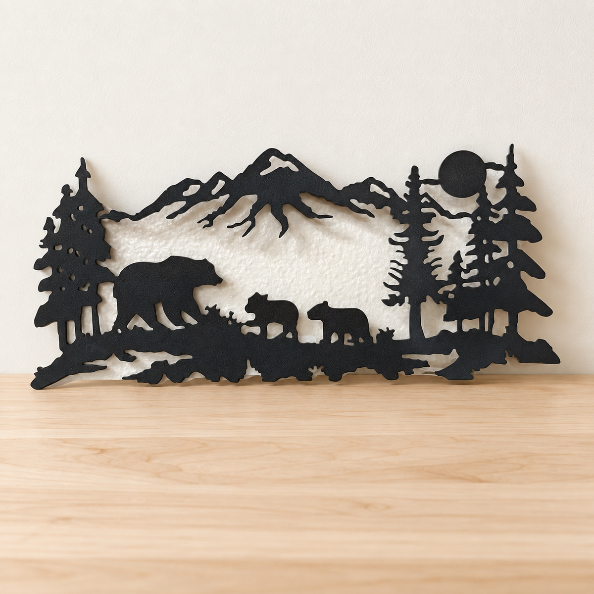 Black bear family silhouette scene with mountains, pine trees and a moon over a pearly white background on a pale wood shelf.