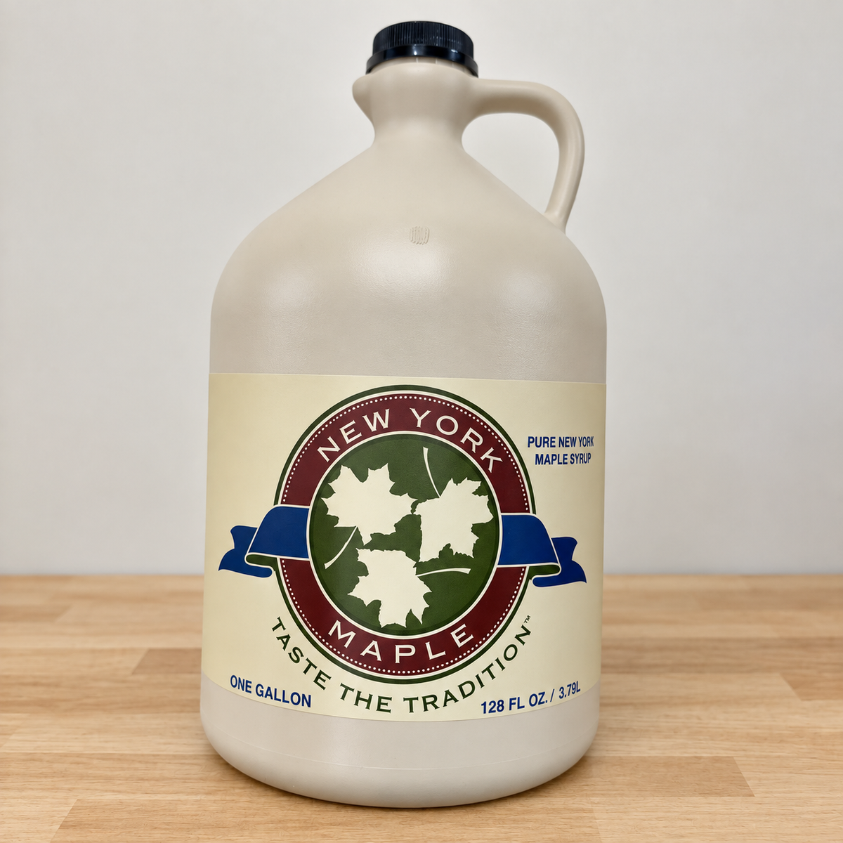 One-gallon beige maple syrup jug with handle, black cap and original New York Maple leaf label, on a pale wood counter.